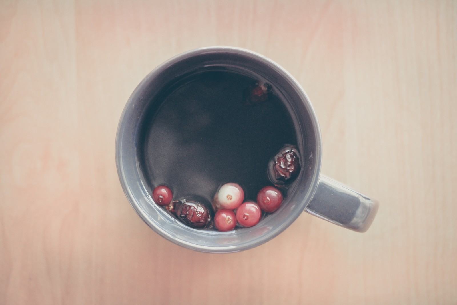 Tea cup from above with a few red berries bobbing in the tea